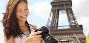 happy woman looking at her camera in front of eiffel tower