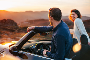 Happy couple looking at sunset from convertible
