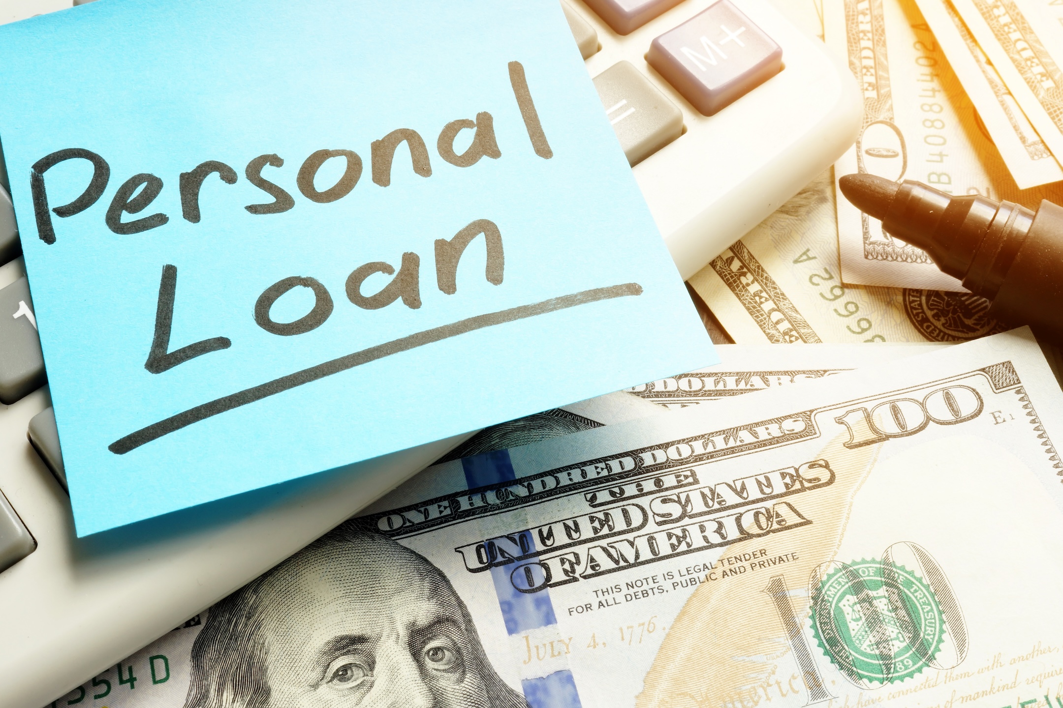 A post it with Personal Loans stuck to a keyboard sitting on paper money laying on a table showcasing reasons for getting a personal loan.