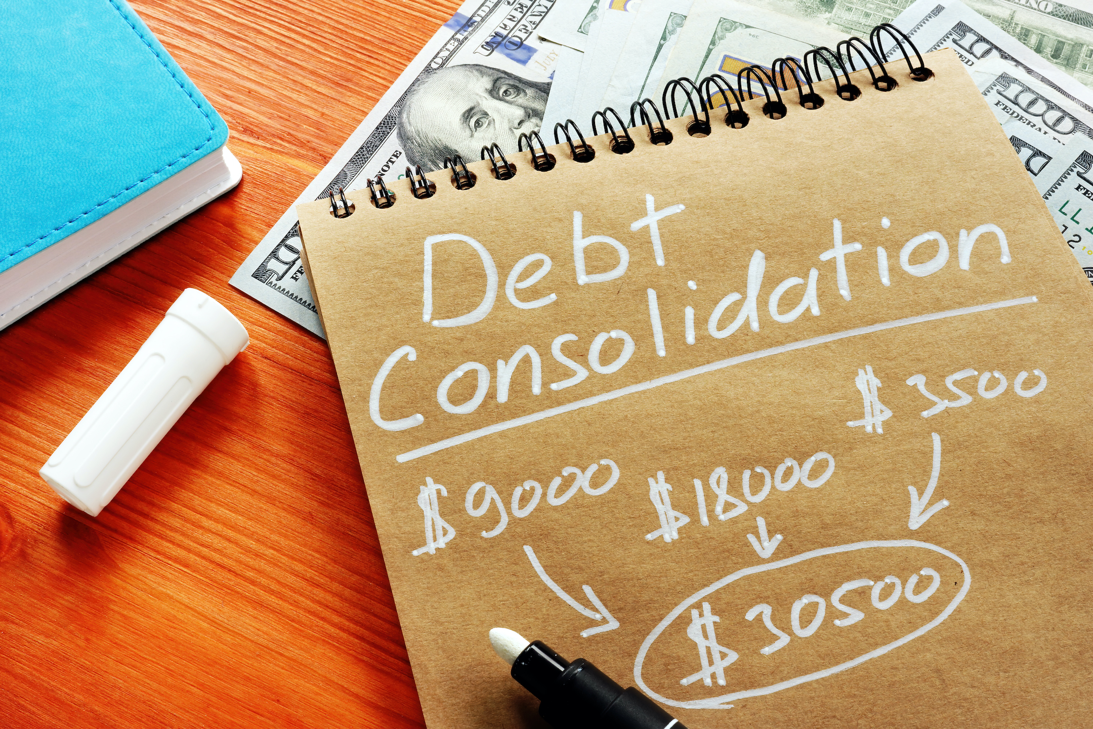 The words debt consolidation is written on a tablet of paper with money around it to showcase credit card refinancing vs debt consolidation when trying to get out of debt.