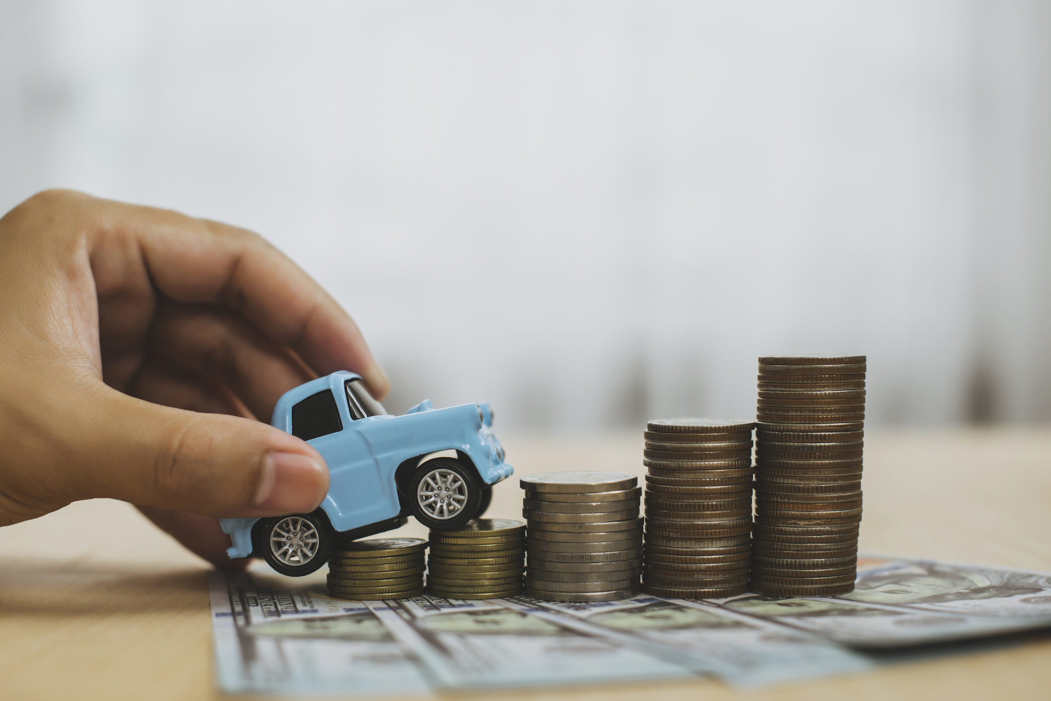 A person with a toy car is climbing stacks of coins showcasing the benefits of refinancing a car.