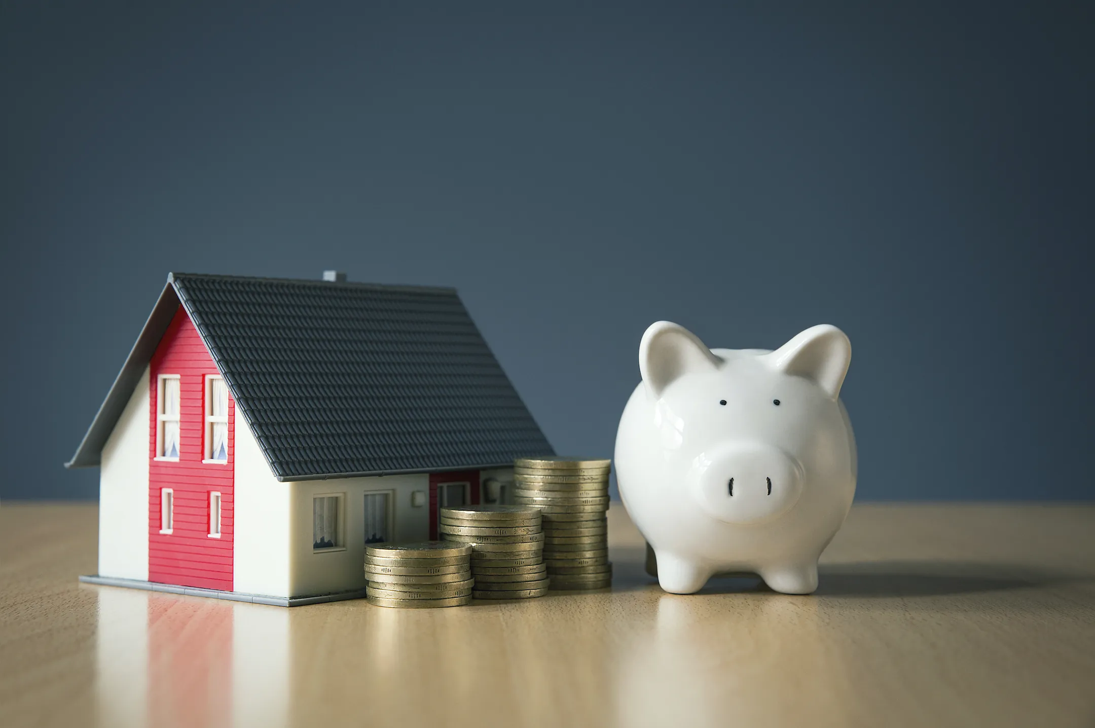 A piggy bank is sitting on a table with coins stacked by a miniature house to showcase home equity loan nj.