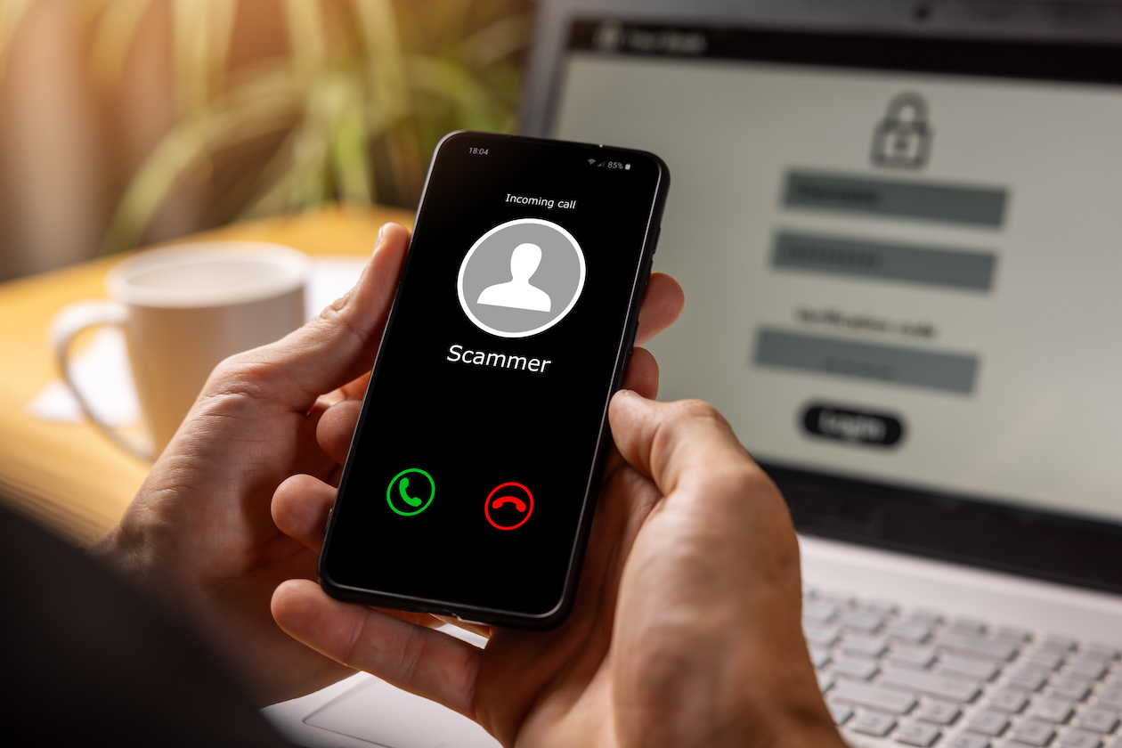 A person is holding a cell phone with an incoming call and the word scammer on the screen indicating bank fraud.