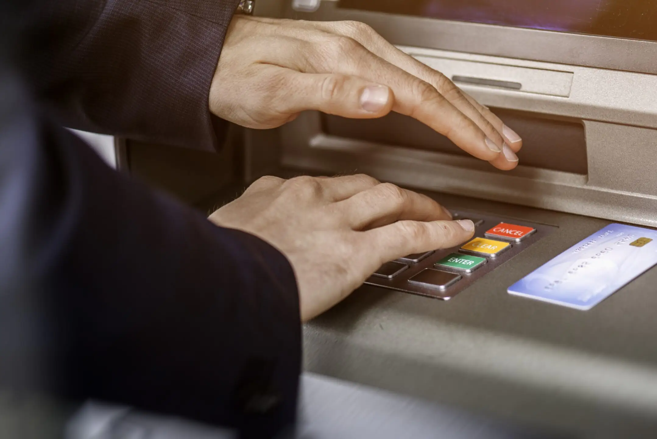 A person about to enter their PIN at an ATM holds one have over the numbers to protect them from ATM scams and keep their money safe.